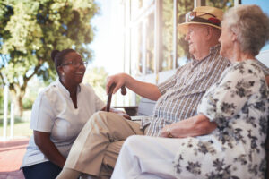 Portrait of senior couple relaxing on a bench outside their retirement home. Caucasian elderly man and woman sitting with female nurse at old age home.