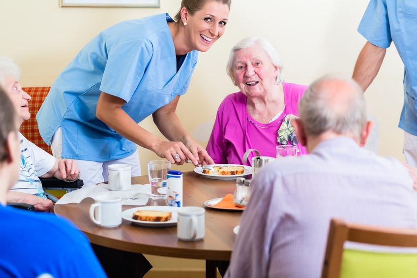 Group of seniors having food in nursing home, a nurse is serving