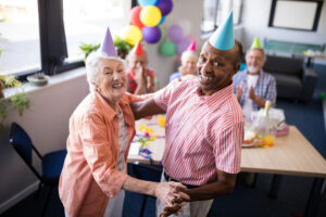 Portrait of happy senior couple dancing by table at birthday party